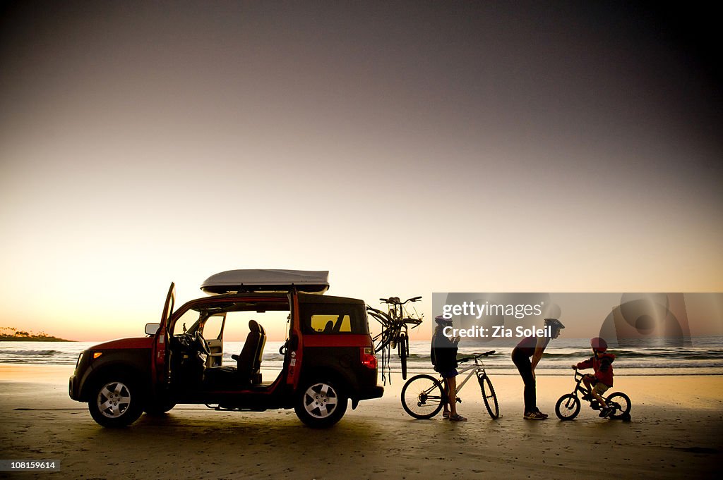 Family on beach with bikes and car, sunset