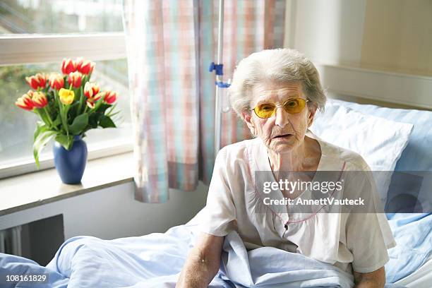 senior woman sitting in hospital bed by window - hospital bed stock pictures, royalty-free photos & images