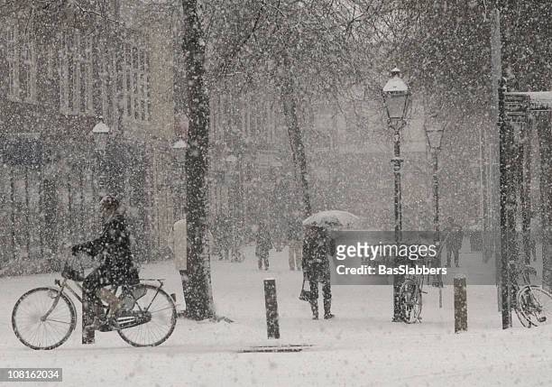 heavy snow falling in town square with people walking - vintage bicycle stock pictures, royalty-free photos & images