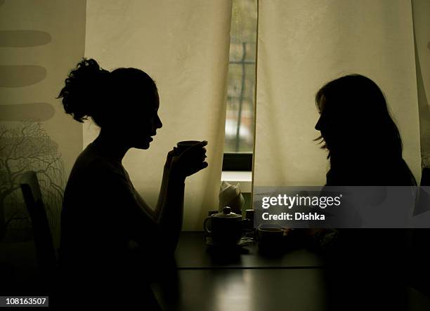 silhouettes of two women drinking tea in cafe - fluisteren stockfoto's en -beelden