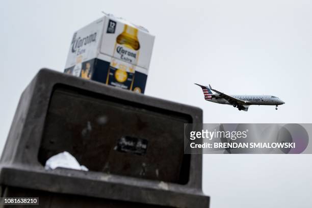 An American Airlines plane passes over an overflowing trash can with a Corona Beer box on it in Gravelly Point Park while landing at Ronald Reagan...