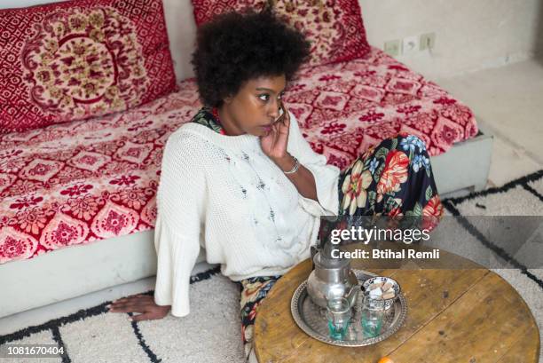 woman sitting in her room and talking on the phone while having a cup of tea - morocco interior ストックフォトと画像