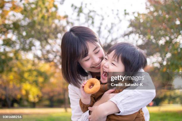 giovane madre e figlio che mangiano ciambella nel parco pubblico con pieno di divertimento - eating donuts foto e immagini stock