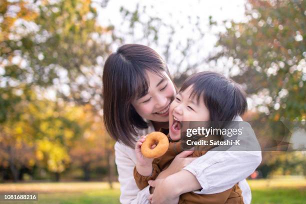 jonge moeder en zoon eten donut in openbaar park met vol plezier - eating donuts stockfoto's en -beelden