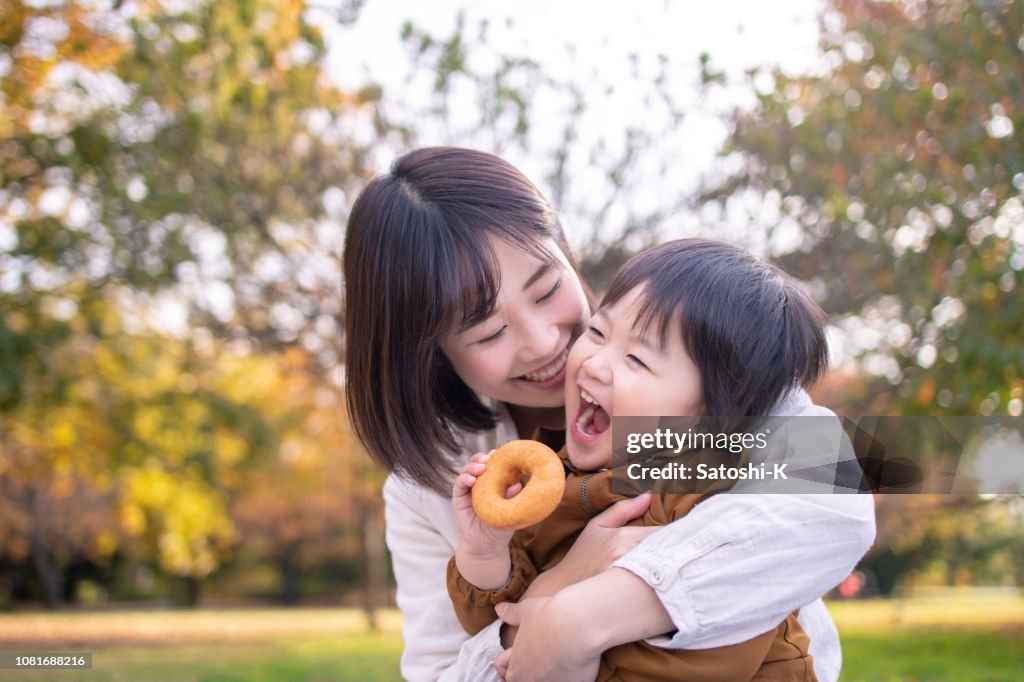 Young mother and son eating doughnut in public park with full of fun