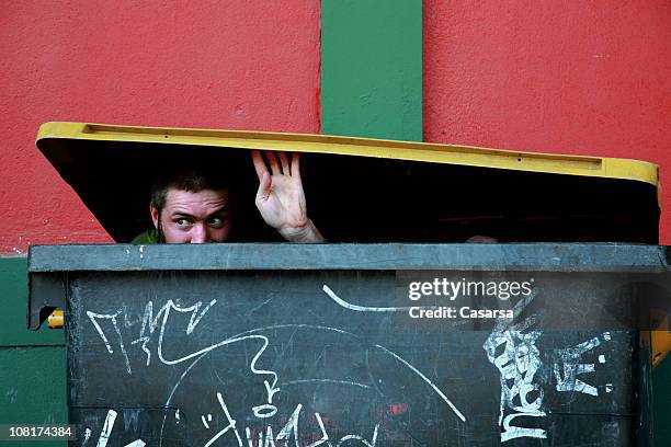 junger mann versteckt in den müll-container und schaut - müllcontainer stock-fotos und bilder