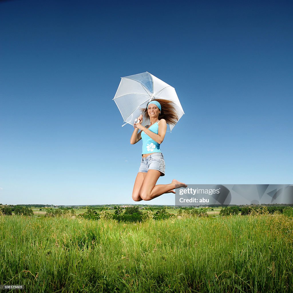 Junge Frau springen im sonnigen Feld und hält Regenschirm