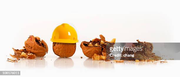 walnut wearing hard hat beside other crushed nuts - losbreken stockfoto's en -beelden