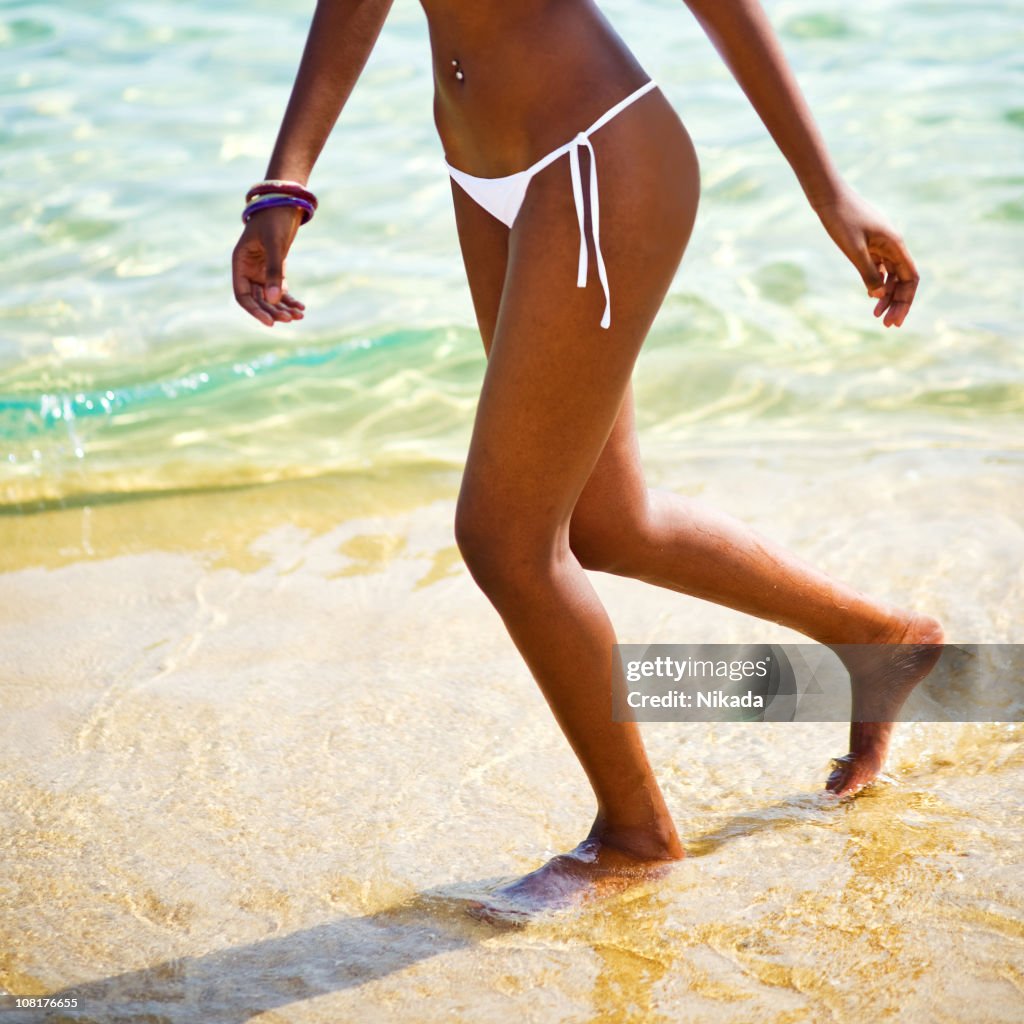 Jovem mulher de pernas a caminhar ao longo da praia