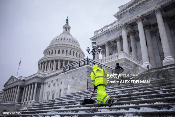 Workers from the Architect of the US Capitol clear snow from the steps of the Capitol as snow continues to fall in Washington, DC on January 13,...