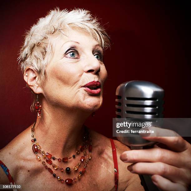 senior woman singing into retro jazz microphone - speakeasy interior stock pictures, royalty-free photos & images