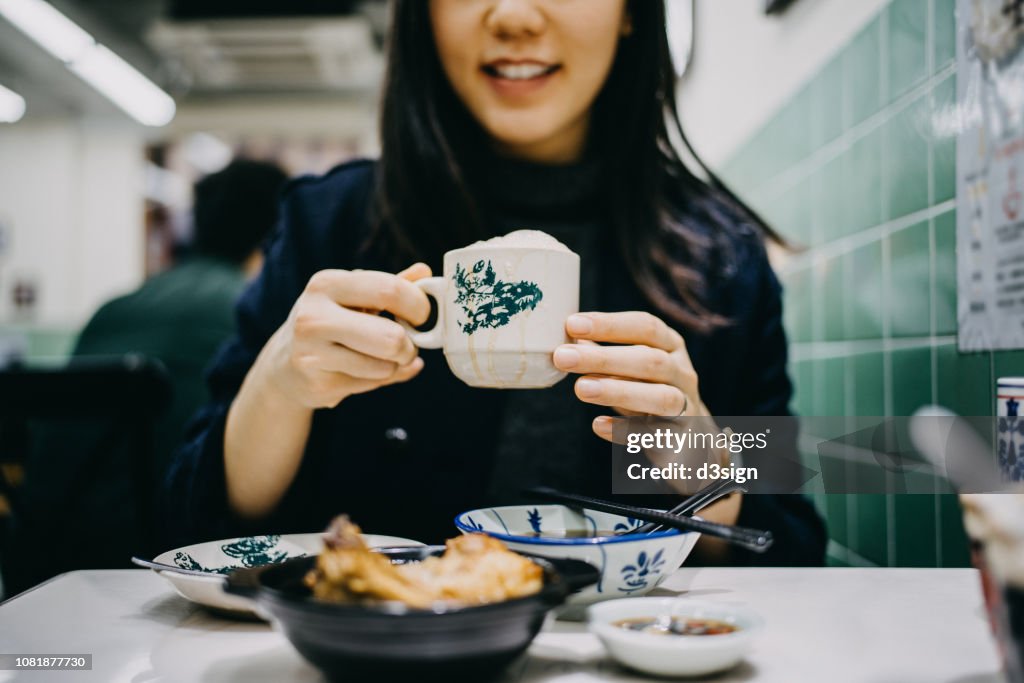 Joyful young woman enjoying Bakuteh and Teh Tarik in a traditional restaurant