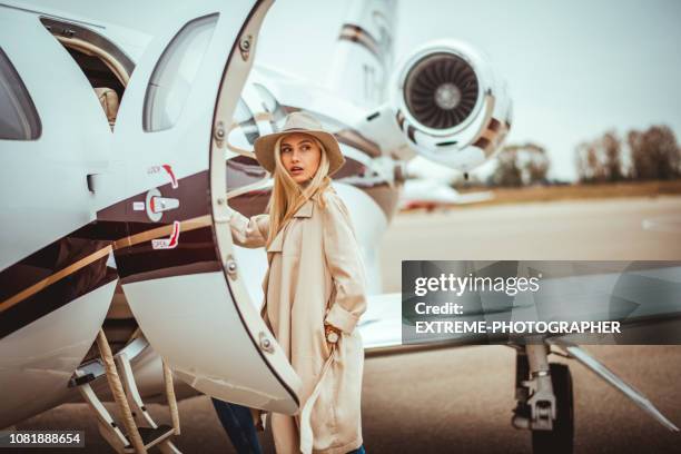 jonge rijke blonde vrouwelijke over haar schouder kijken bij het invoeren van een privé vliegtuig geparkeerd op een luchthaven asfalt - vip stockfoto's en -beelden