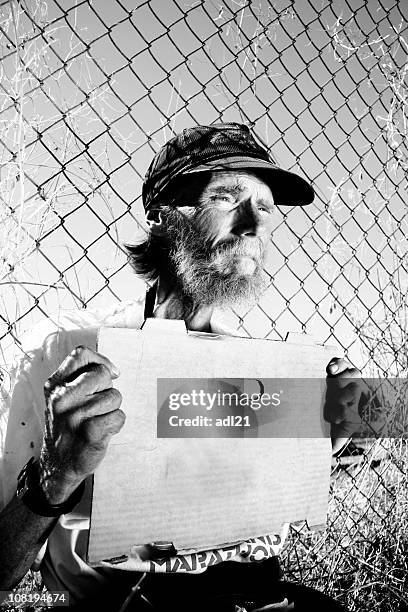 homeless man holding blank sign sitting against fence - metal fence stock pictures, royalty-free photos & images
