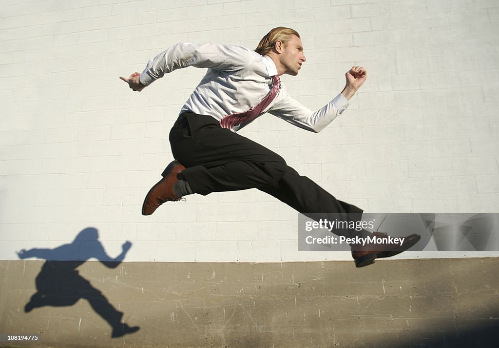 Businessman Jumping Outdoors Across White Wall with Shadow