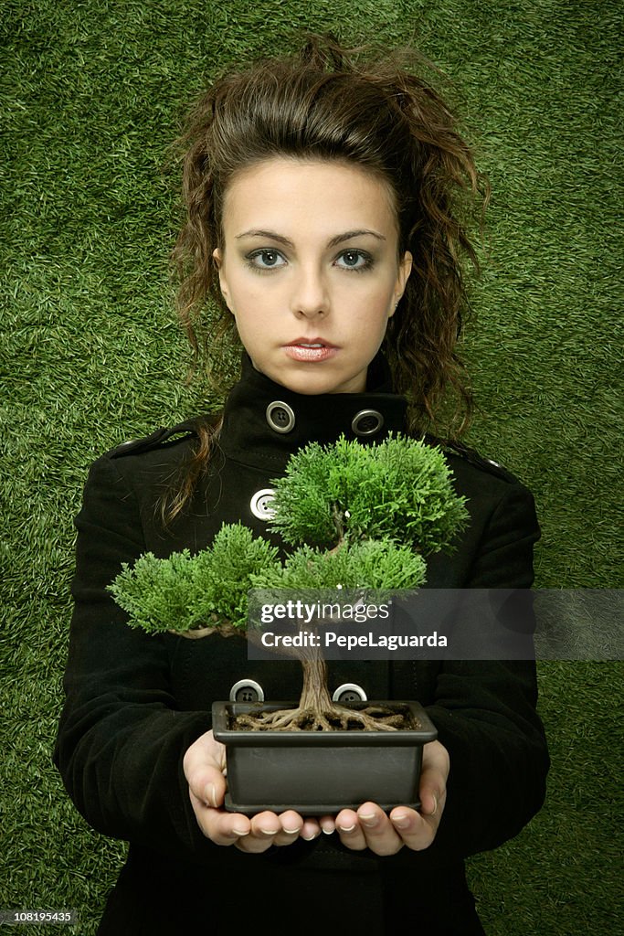 Young Woman Holding Bonsai Tree Against Grass Background