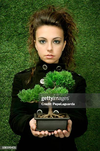 young woman holding bonsai tree against grass background - ecologist stock pictures, royalty-free photos & images