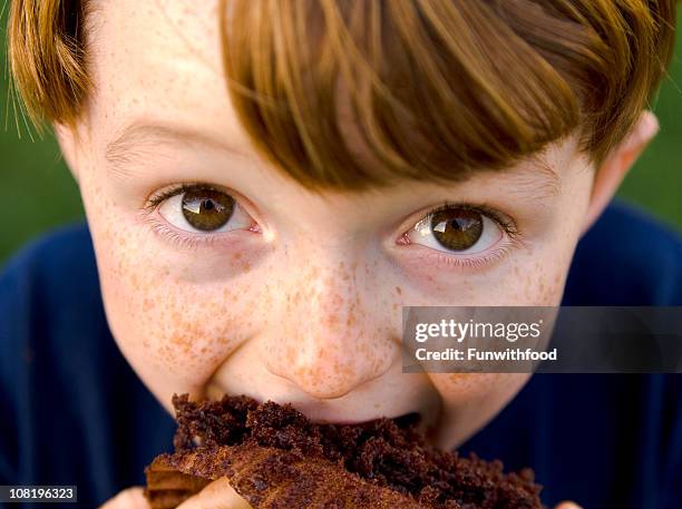 boy redhead & funny freckle face child eating unhealthy chocolate cupcake - taart stockfoto's en -beelden