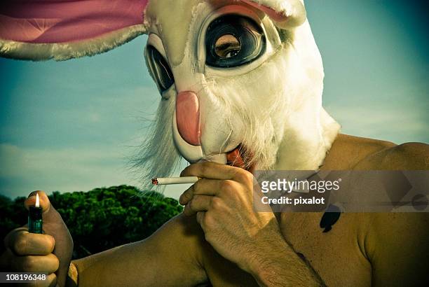 hombre usando la máscara de conejo iluminación de cigarrillos - easter bunny fotografías e imágenes de stock
