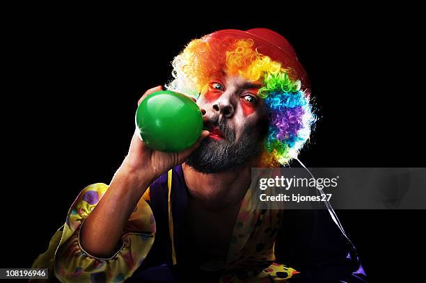 creepy looking clown blowing up balloon on black background - psychotic stock pictures, royalty-free photos & images