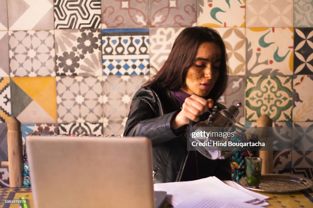 Young women pouring tea front of her computer