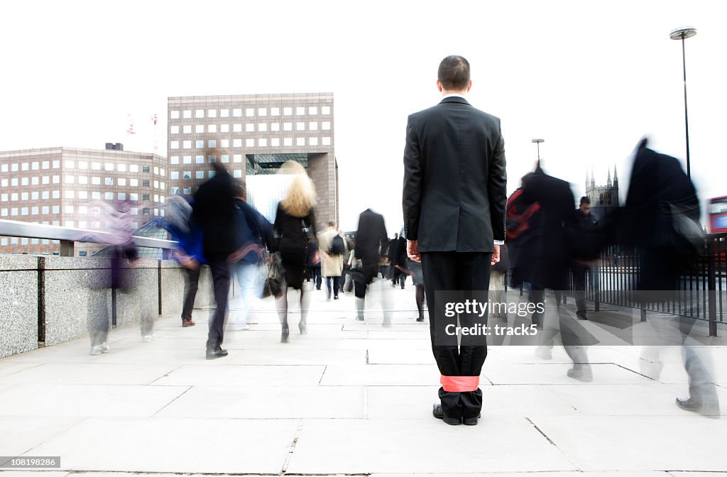 Businessman with his legs tied together in a crowd