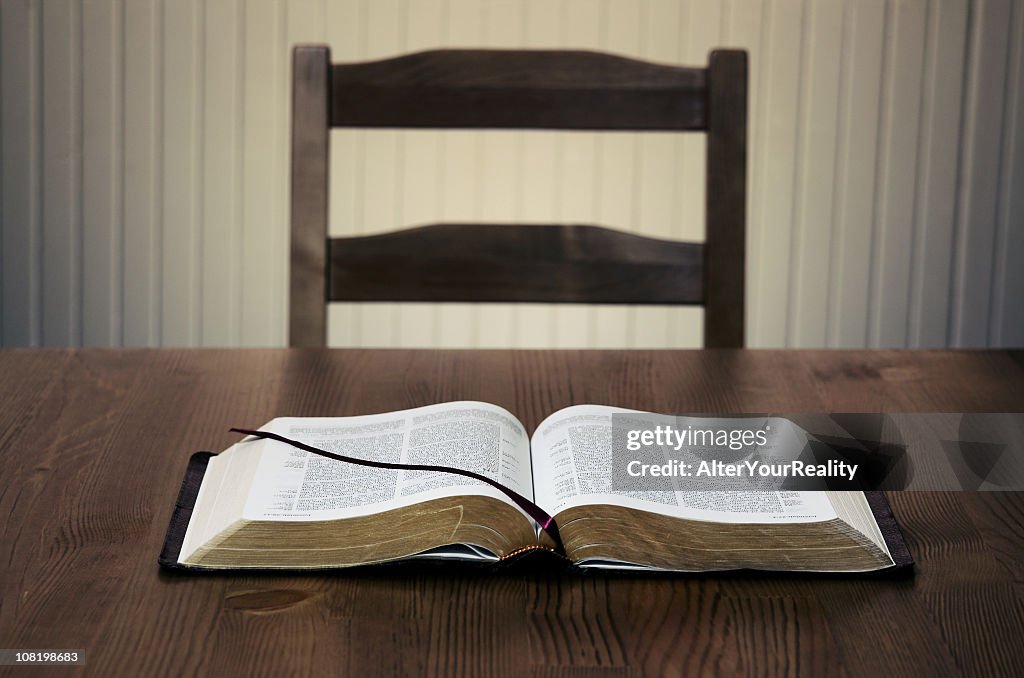 Bible sitting open on a table in front of an empty chair