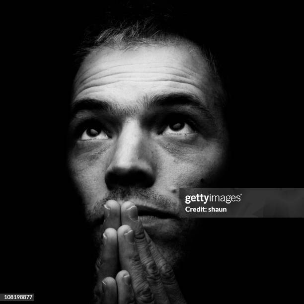 portrait of man holding hands in prayer, black and white - clair obscur stockfoto's en -beelden