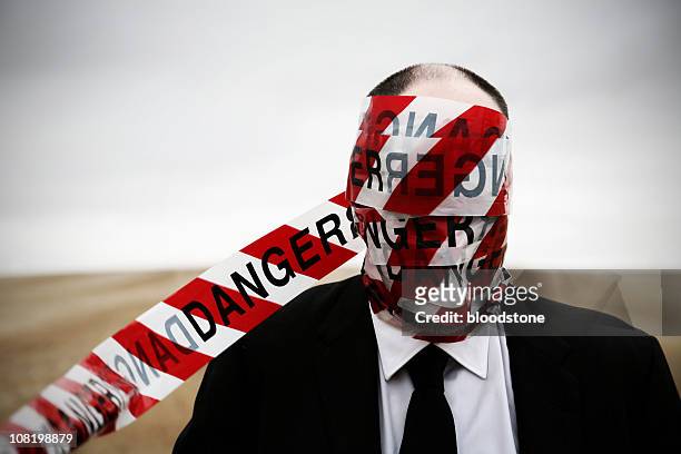 businessman with "danger" cordon tape wrapped around head - bureaucracy stock pictures, royalty-free photos & images