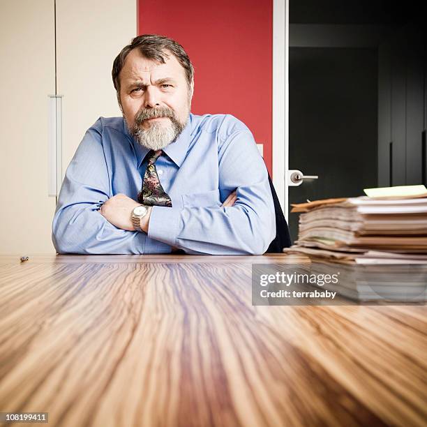 sérieux homme d'affaires, assis au bureau avec les documents - vieux grincheux photos et images de collection