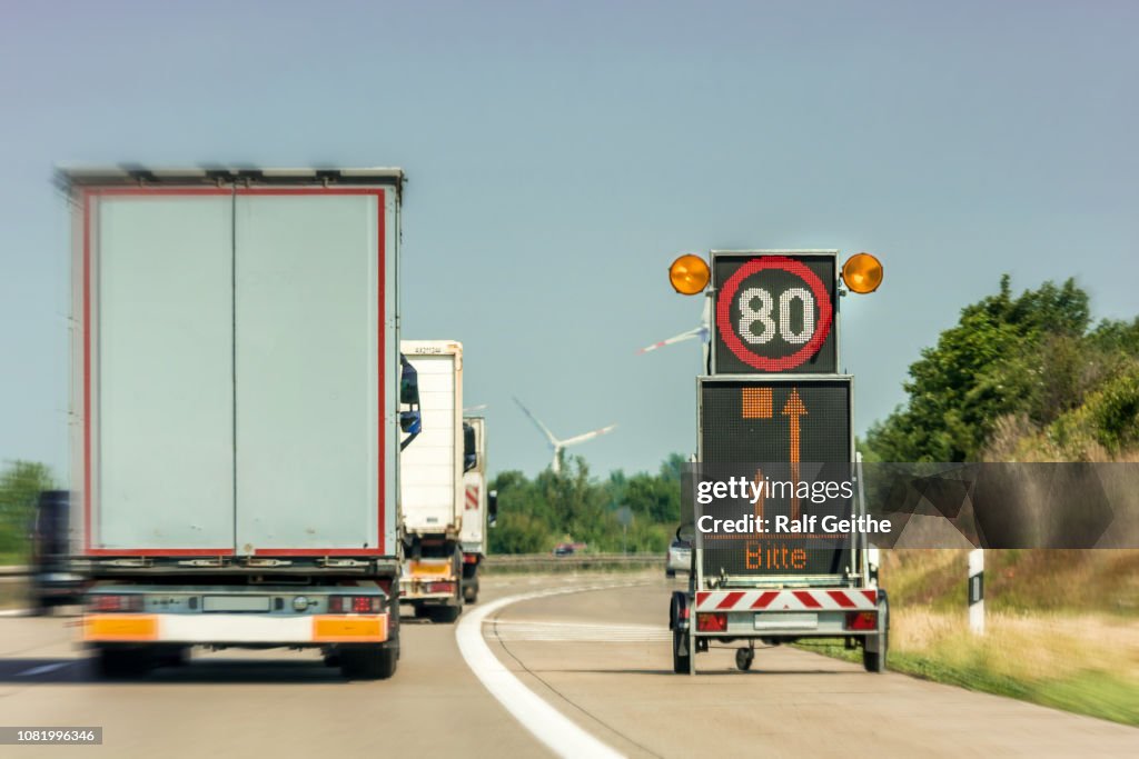 Panneau de signalisation numérique indiquant un chantier de construction d’autoroute avec le mot allemand pour « please » à l’écran