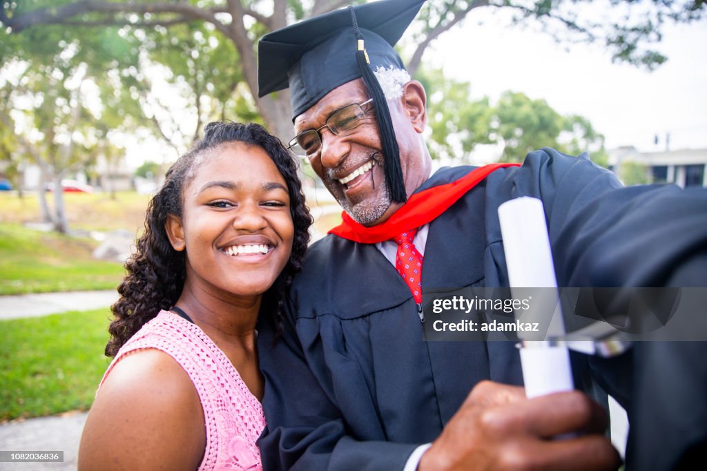 Senior black man at graduation taking a selfie with his daughter