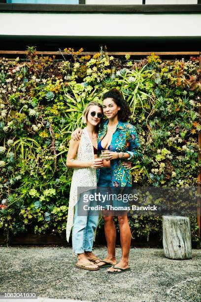 Portrait of smiling female couple embracing in front of living wall
