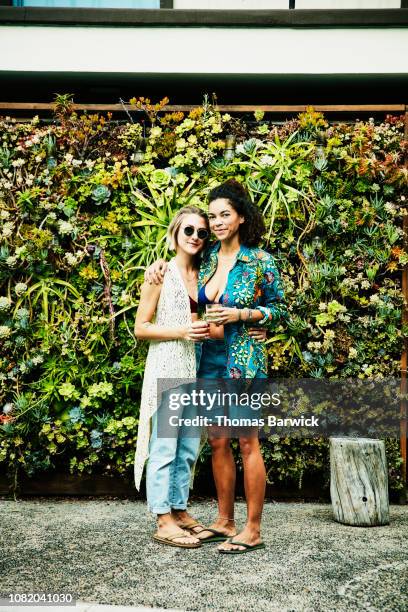 portrait of smiling female couple embracing in front of living wall - decolleté stockfoto's en -beelden