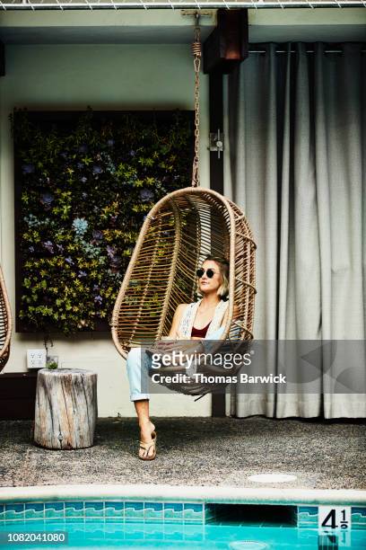woman relaxing in hanging chair by pool - hanging chair stock pictures, royalty-free photos & images