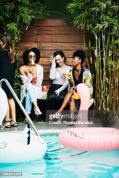 laughing friends sharing drinks while sitting by pool during party - friends poolside stock pictures, royalty-free photos & images