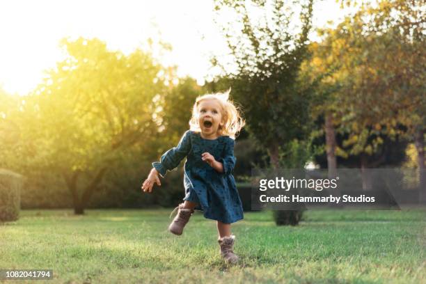 portrait of a happy little girl running by smiling in a public park - baby girls stock pictures, royalty-free photos & images