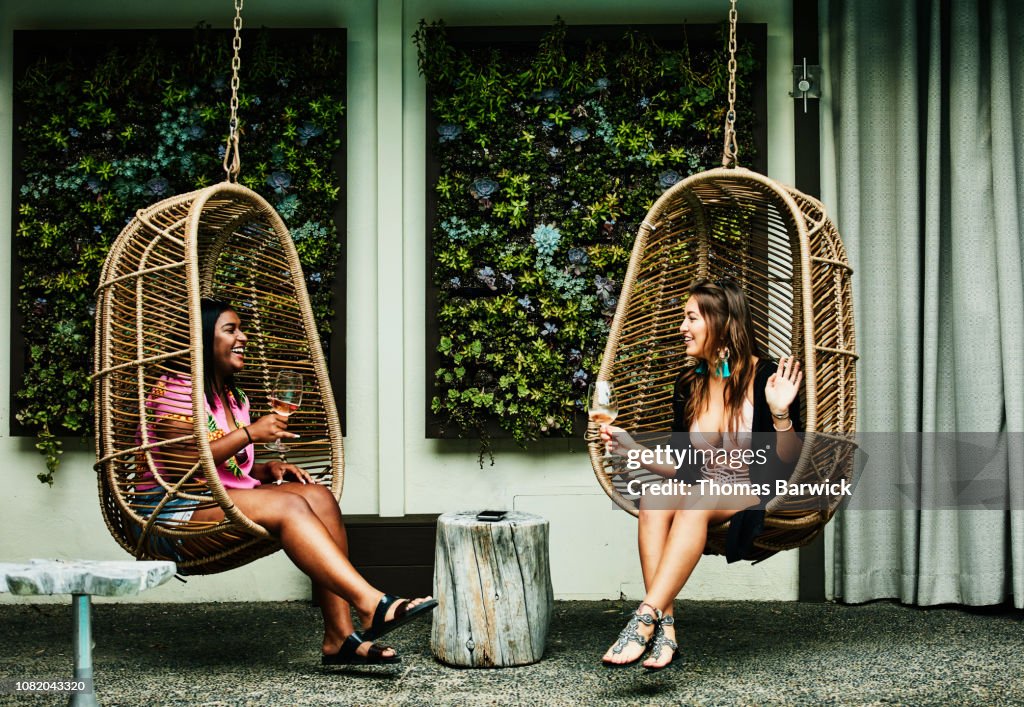 Laughing friends in discussion while sitting in hanging chairs during pool party