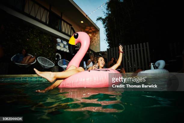woman relaxing in inflatable flamingo during hotel pool party - float imagens e fotografias de stock
