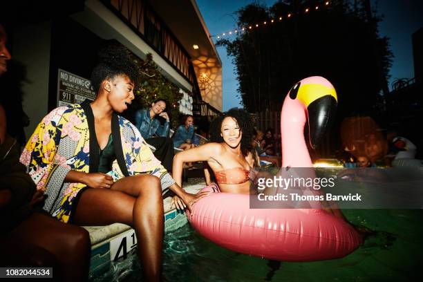 smiling woman sitting in inflatable flamingo in pool during party with friends at hotel - evasión fotografías e imágenes de stock
