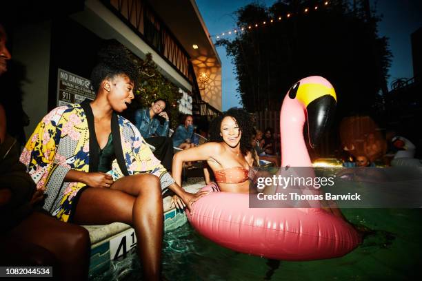 smiling woman sitting in inflatable flamingo in pool during party with friends at hotel - pool party ストックフォトと画像