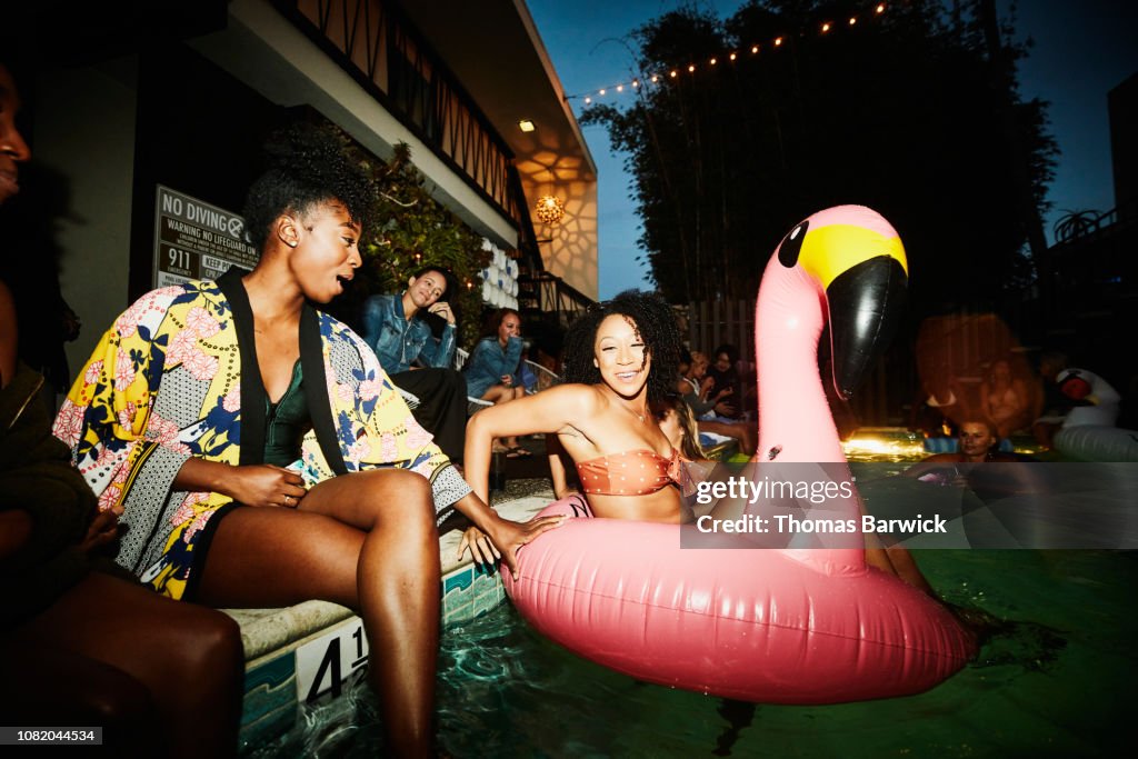 Smiling woman sitting in inflatable flamingo in pool during party with friends at hotel