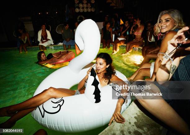 smiling woman enjoying drink while relaxing in inflatable swan during hotel pool party - pool party night stock pictures, royalty-free photos & images