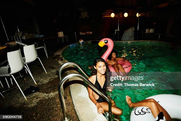 smiling woman sitting on edge of hotel pool during party with friends - pool party night stock pictures, royalty-free photos & images