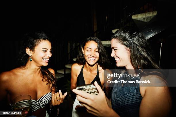 laughing female friends looking at smart phone during party at hotel pool - pool party night stock pictures, royalty-free photos & images