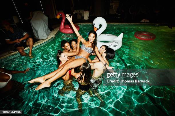 smiling woman being lifted into the air by friends during party in hotel pool - asian woman swimsuit stock-fotos und bilder