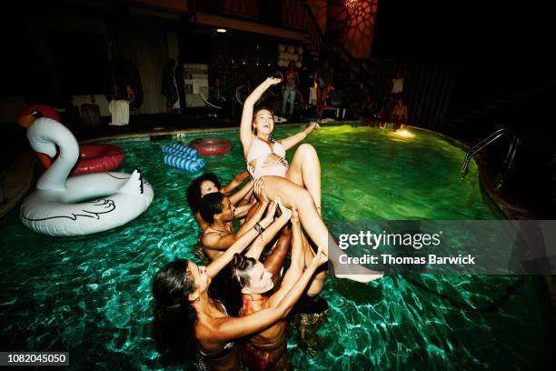 group of friends preparing to throw woman in hotel pool during party - friend mischief stock-fotos und bilder