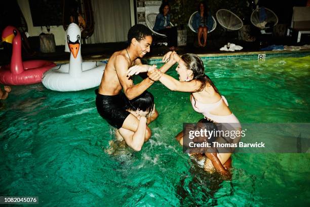 laughing friends having chicken fight in hotel pool during party - pool party night stock pictures, royalty-free photos & images