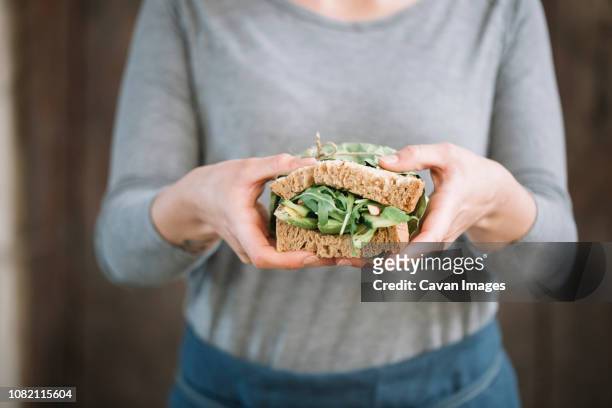 midsection of woman holding sandwich while standing at home - woman sandwich stock-fotos und bilder