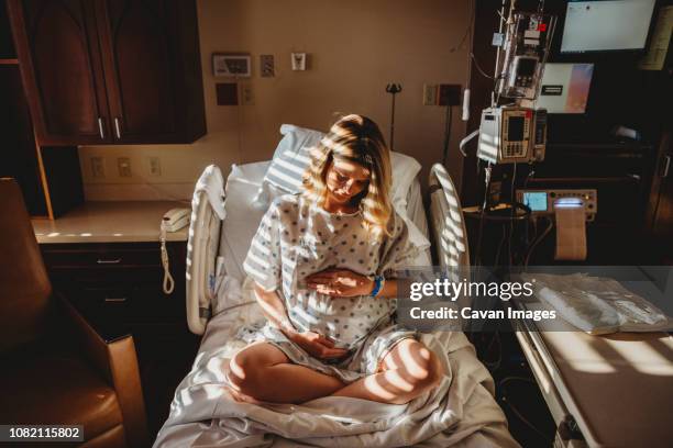 pregnant woman touching stomach while sitting on bed in hospital - labor childbirth - fotografias e filmes do acervo